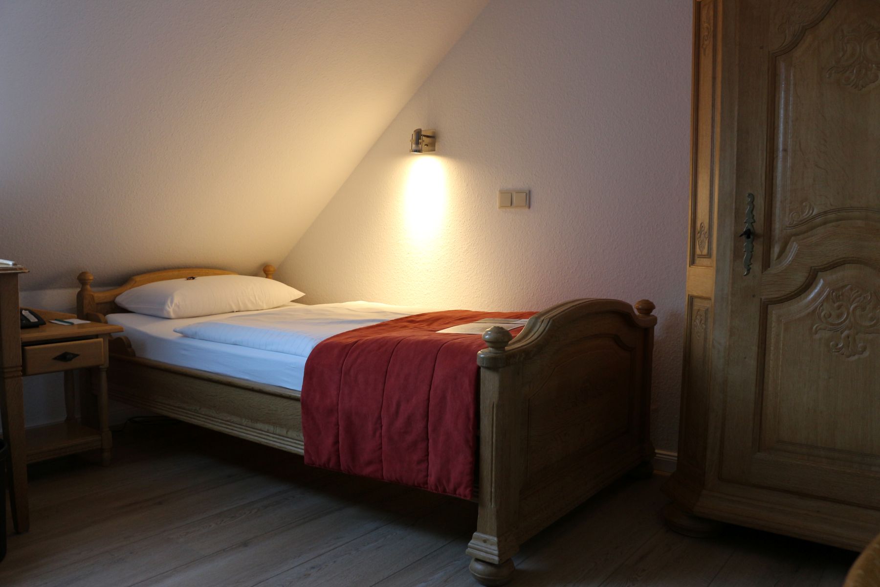 Simply furnished bedroom with wooden bed, red bedspread and closet under sloping ceiling