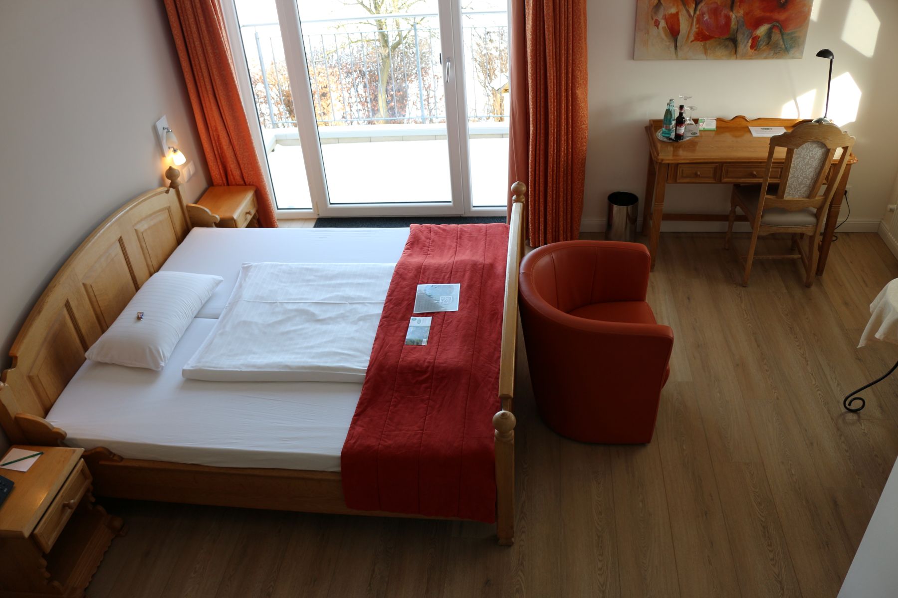 Helles Deluxe Zimmer mit Doppelbett, rotem Sessel, Schreibtisch und Balkonzugang mit großen Fenstern