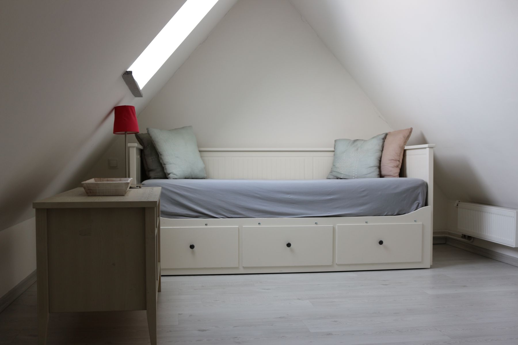 Gemütlicher Schlafbereich unter Dachschräge mit Tagesbett, Kissen und Dachfenster, ruhig und modern