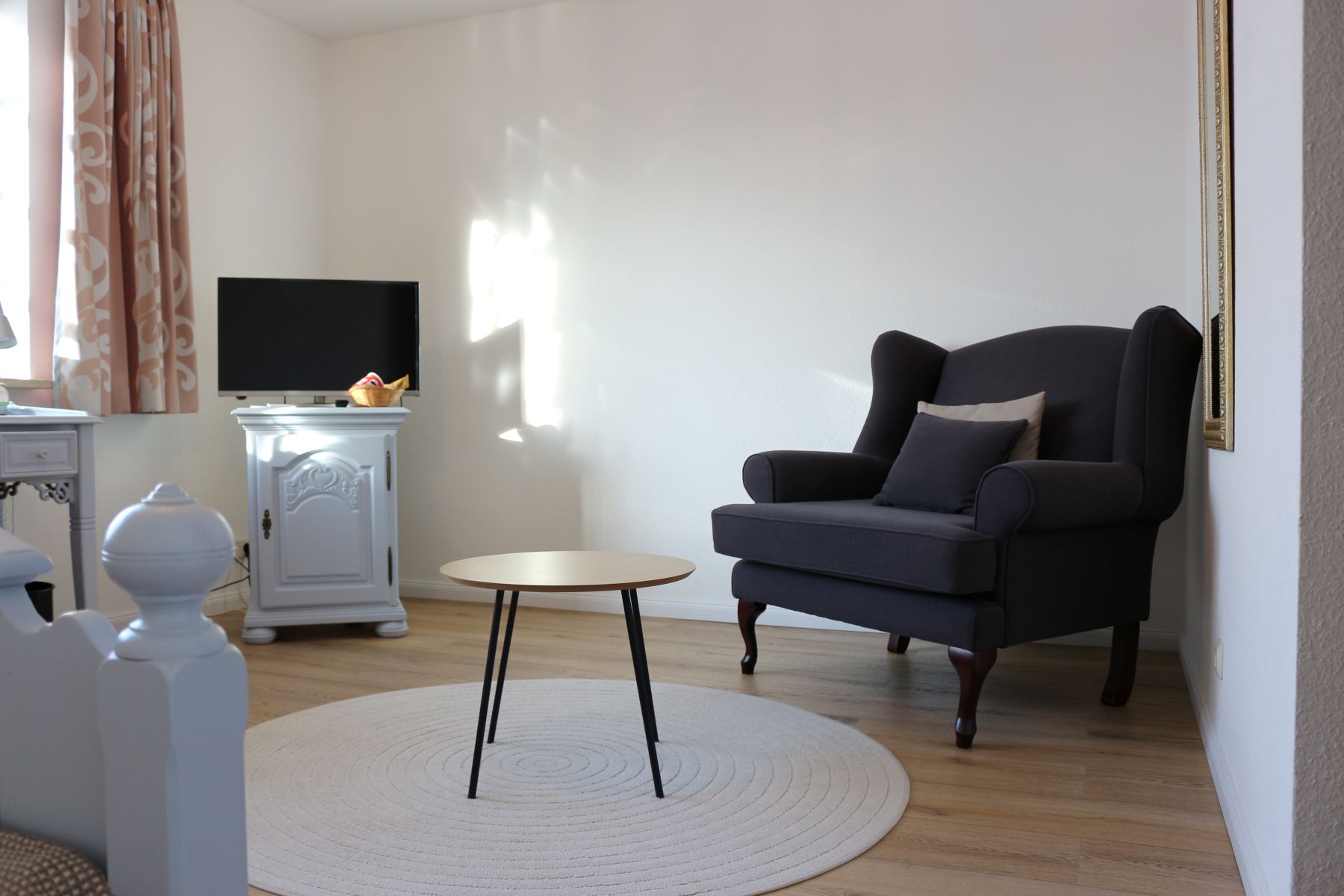Cozy sitting area in the hotel room with armchair, side table and TV on chest of drawers