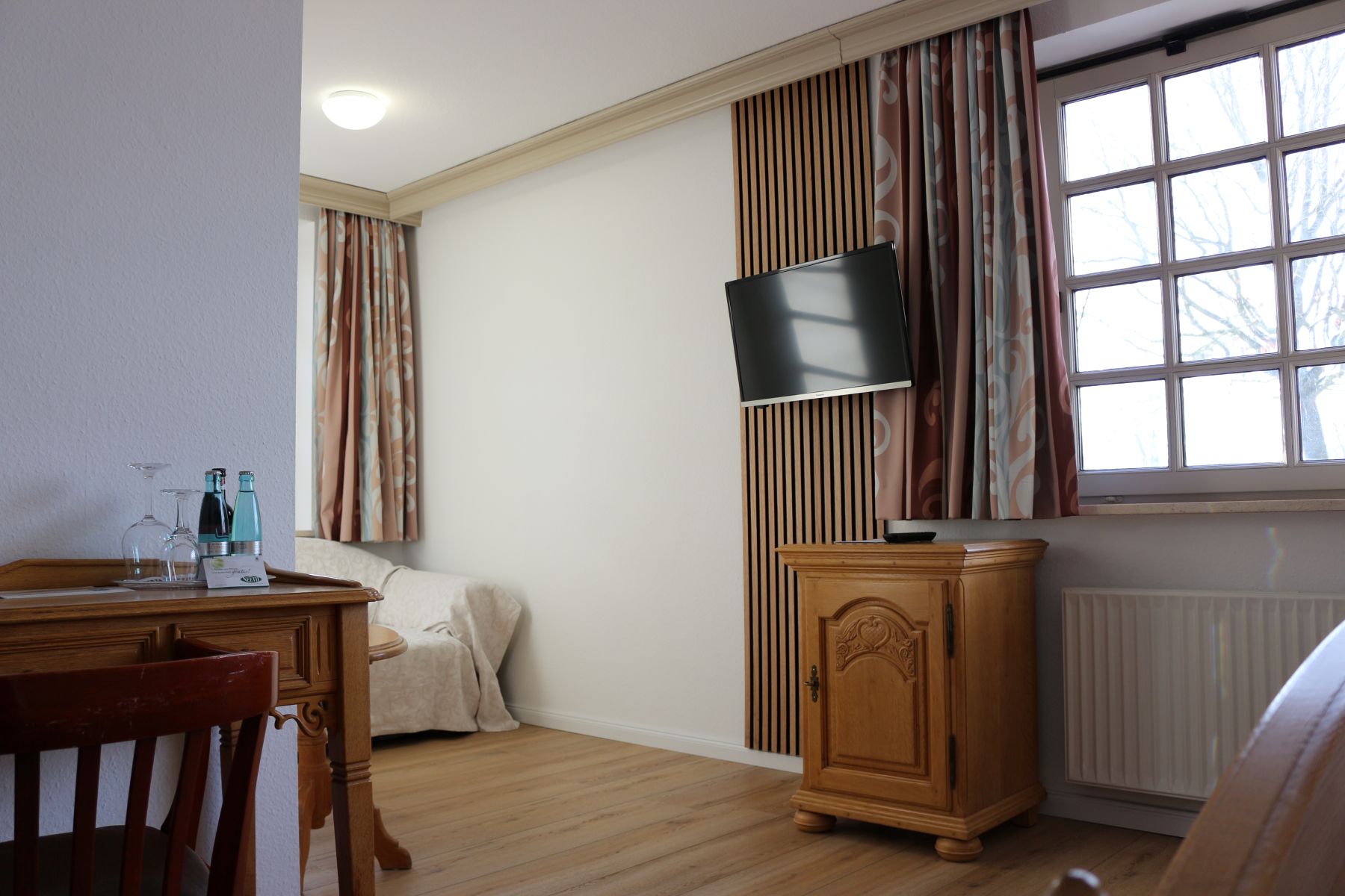 Hotel room with TV, wooden furniture, desk and window with curtains