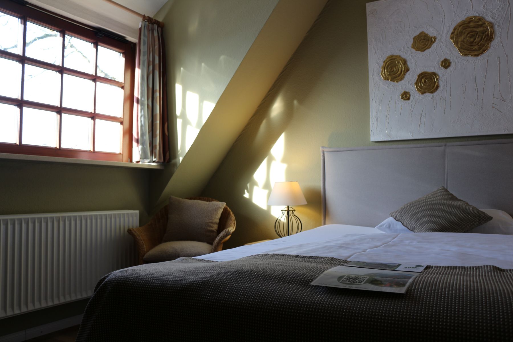 Bright hotel room with double bed, cozy armchair and sloping roof, natural light through windows