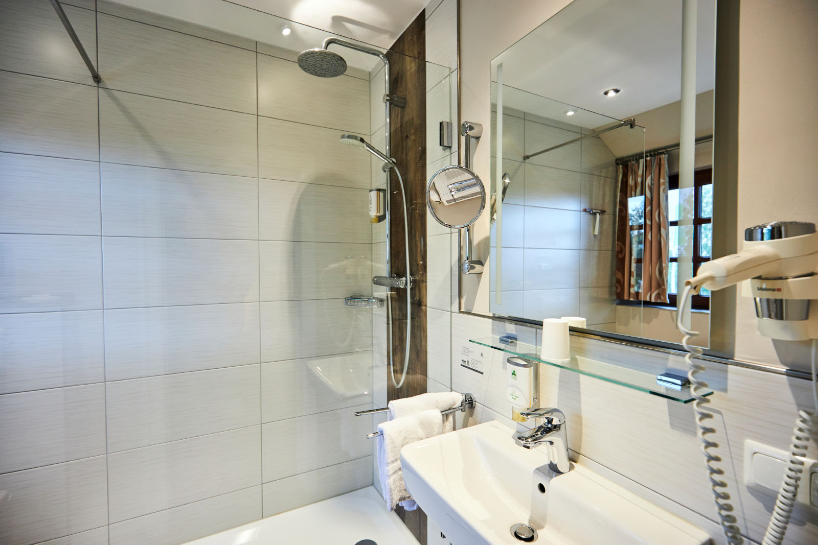 Modern bathroom with walk-in glass shower, washbasin, large mirror and bright tiled look