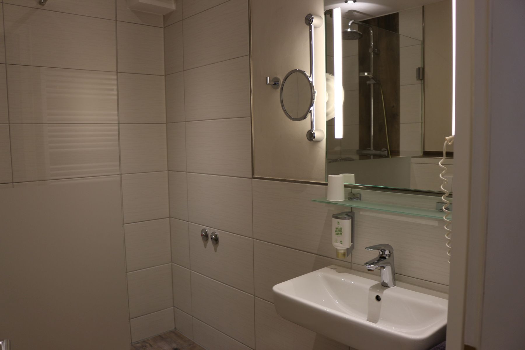 Contemporary bathroom with illuminated mirror, washbasin and tiled shower