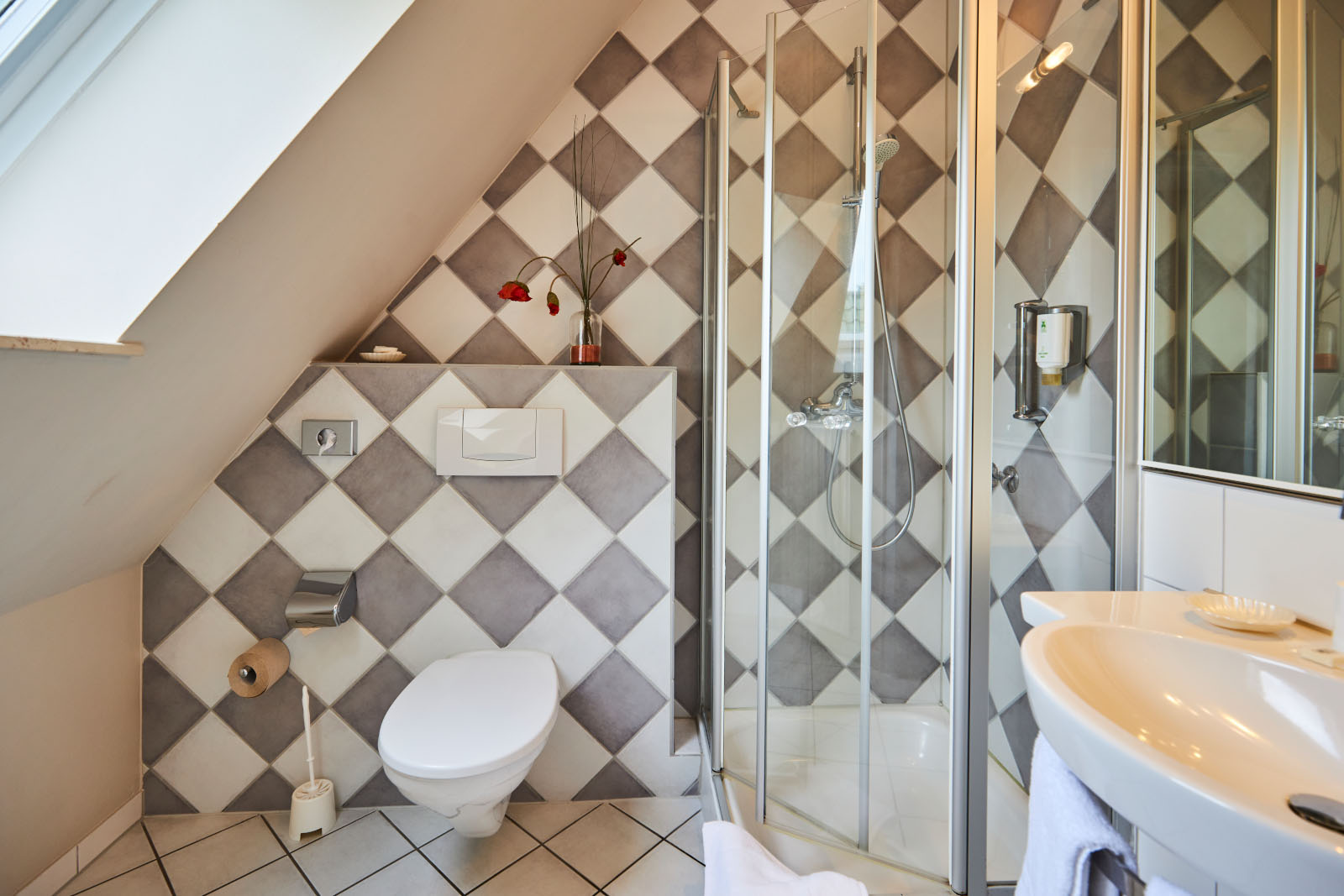 Modernes Badezimmer mit Duschkabine, WC und Waschbecken unter Dachschräge, dekorative Fliesenoptik